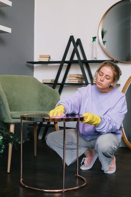 A person is rolling out a beige and brown patterned carpet onto a wooden floor in a living room, with another individual helping to smooth it out. The room features hardwood flooring, and the carpet a